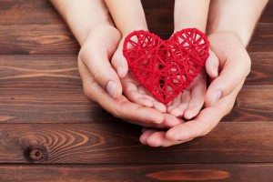62038274 - adult and child holding red heart in hands over a wooden table. family relationships, health care, pediatric cardiology concept.